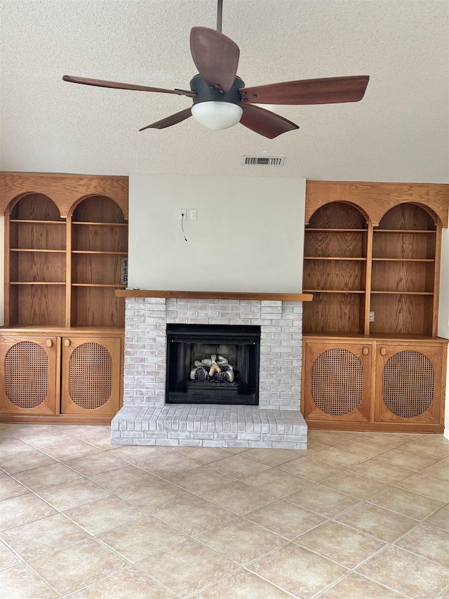 unfurnished living room featuring visible vents, ceiling fan, built in features, a fireplace, and a textured ceiling