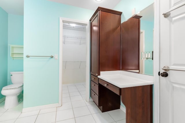 bathroom with vanity, baseboards, tile patterned flooring, a walk in closet, and toilet