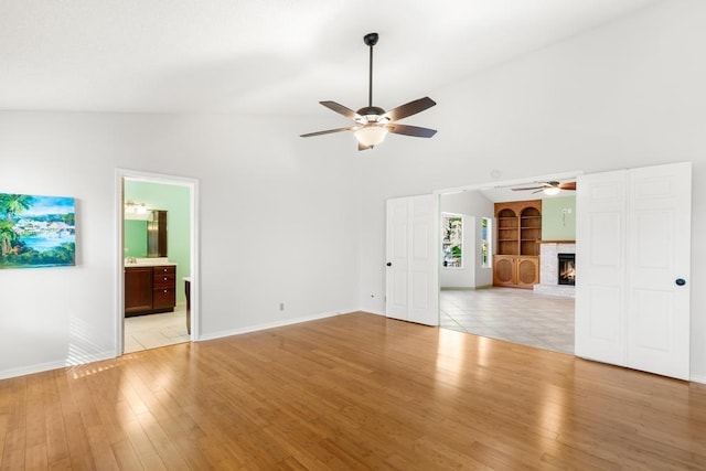 unfurnished living room with light wood finished floors, built in features, a fireplace, and a ceiling fan