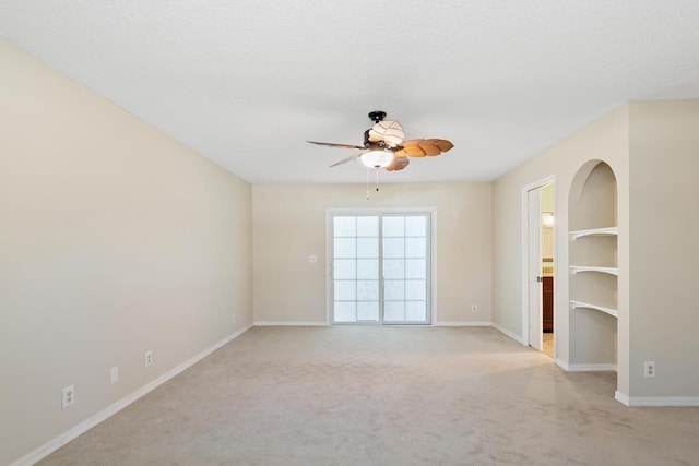 spare room with arched walkways, light colored carpet, baseboards, and ceiling fan