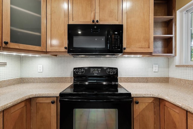 kitchen with tasteful backsplash, glass insert cabinets, light stone counters, black appliances, and open shelves