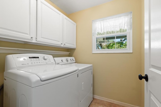 clothes washing area with light tile patterned flooring, cabinet space, baseboards, and washing machine and clothes dryer