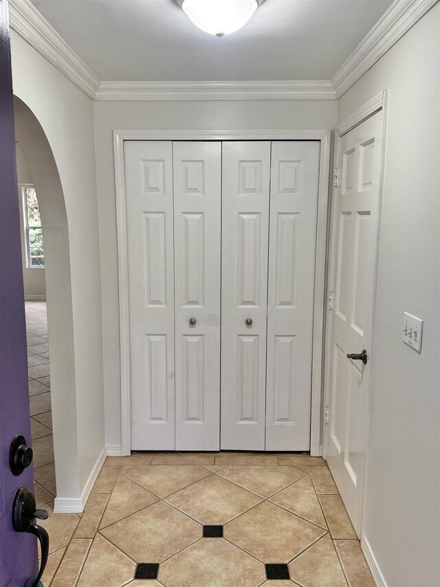 entryway featuring arched walkways, crown molding, baseboards, and light tile patterned flooring