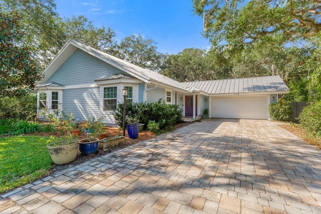 ranch-style house with fence, metal roof, decorative driveway, an attached garage, and a standing seam roof