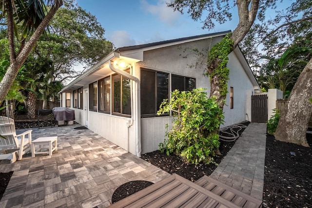 view of property exterior featuring a sunroom, a patio area, fence, and stucco siding