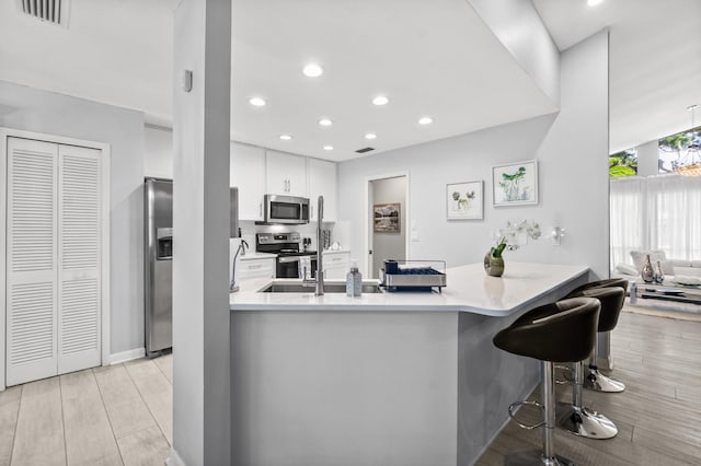 kitchen with visible vents, appliances with stainless steel finishes, light wood-style floors, a peninsula, and a kitchen breakfast bar