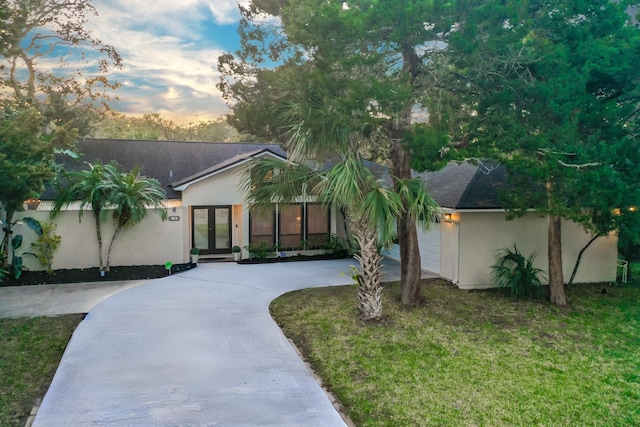 view of front facade featuring driveway, french doors, a lawn, roof with shingles, and stucco siding