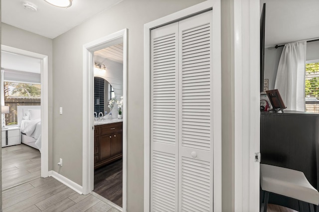 hall featuring light wood-style floors, a sink, and baseboards