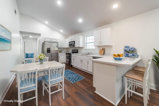 kitchen with stainless steel appliances, white cabinets, vaulted ceiling, a peninsula, and a kitchen bar