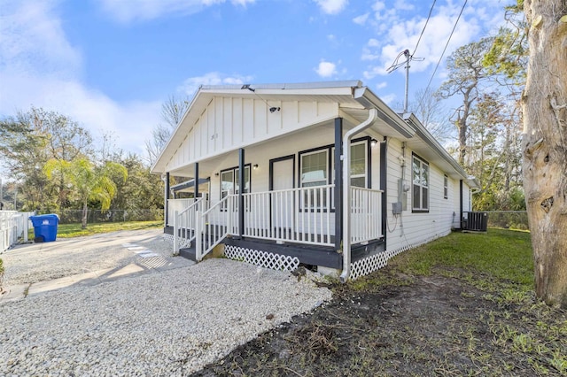 view of front of home with gravel driveway, covered porch, board and batten siding, fence, and cooling unit