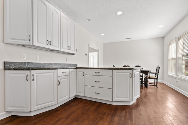 kitchen featuring dark wood-style flooring, white cabinetry, a textured ceiling, a peninsula, and baseboards