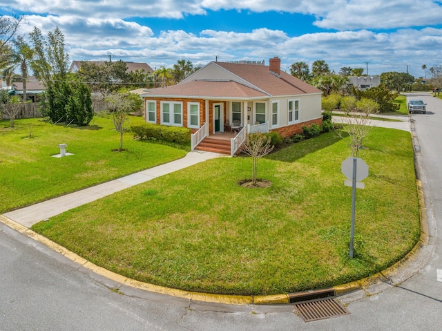 view of front of home with a porch, brick siding, a chimney, and a front lawn