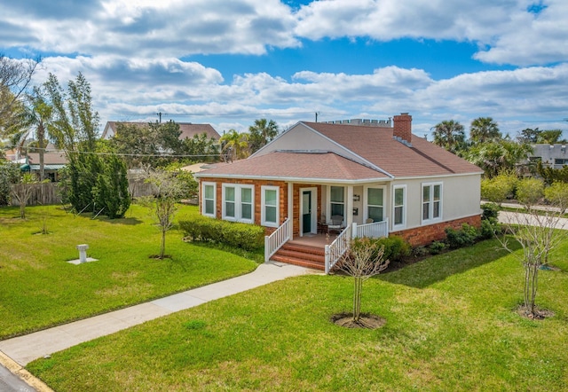 view of front of house with a porch, brick siding, a chimney, and a front lawn