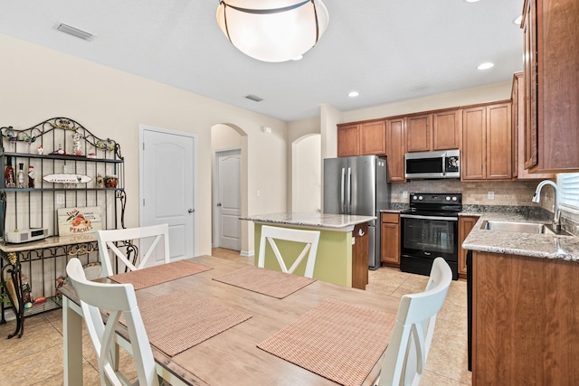 kitchen featuring sink, a center island, light stone counters, backsplash, and appliances with stainless steel finishes