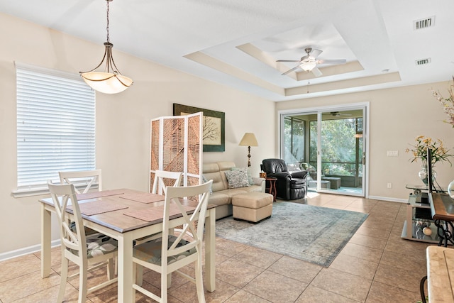 tiled dining area with ceiling fan and a raised ceiling