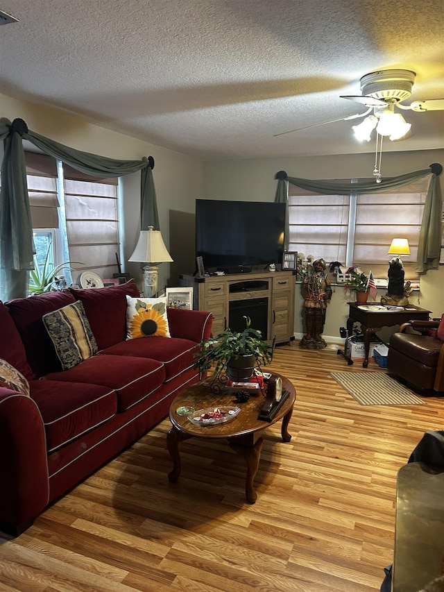 living room featuring ceiling fan, a textured ceiling, and light hardwood / wood-style flooring