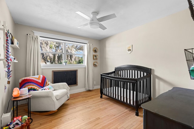 bedroom featuring ceiling fan, light wood-style flooring, baseboards, and a crib