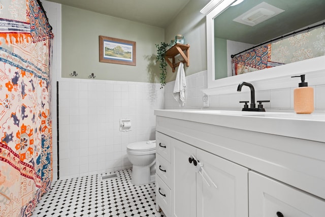 bathroom with tile walls, visible vents, toilet, wainscoting, and vanity