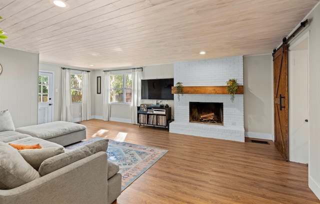 living room featuring a barn door, visible vents, wood ceiling, wood finished floors, and a fireplace