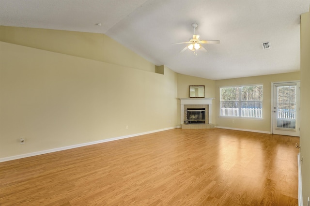 unfurnished living room with visible vents, light wood finished floors, lofted ceiling, ceiling fan, and a tile fireplace