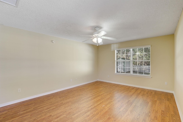 spare room featuring light wood finished floors, visible vents, baseboards, ceiling fan, and a textured ceiling