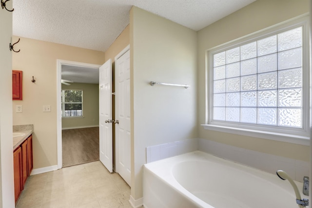 bathroom with baseboards, a textured ceiling, vanity, and a garden tub