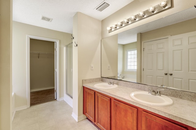 bathroom with a textured ceiling, a shower stall, visible vents, and a sink