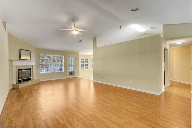 unfurnished living room with a tiled fireplace, light hardwood / wood-style flooring, vaulted ceiling, ceiling fan, and a textured ceiling