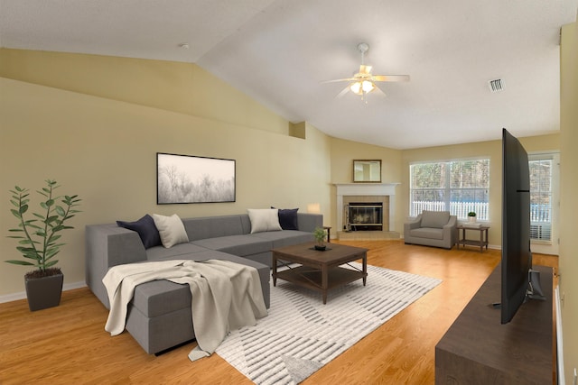 living area featuring a ceiling fan, visible vents, light wood finished floors, lofted ceiling, and a tiled fireplace