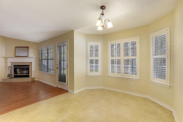 unfurnished dining area featuring a textured ceiling, a tile fireplace, baseboards, and an inviting chandelier