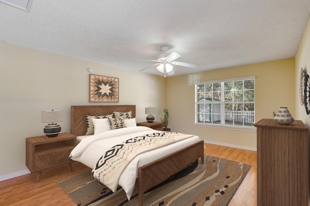 bedroom with visible vents, baseboards, light wood-style flooring, a textured ceiling, and a ceiling fan