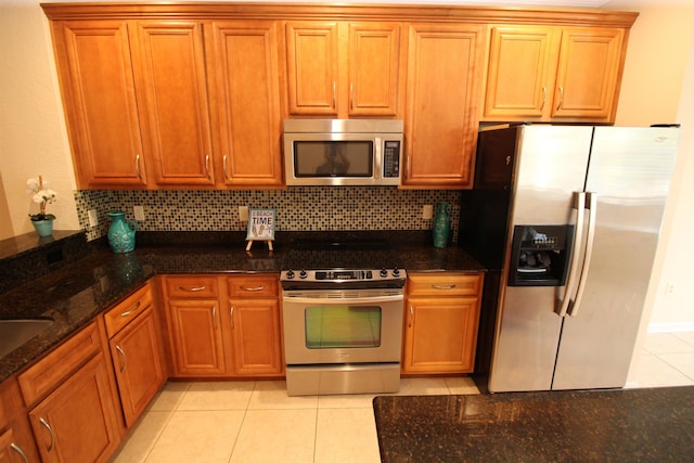 kitchen with tasteful backsplash, light tile patterned floors, brown cabinetry, dark stone counters, and stainless steel appliances