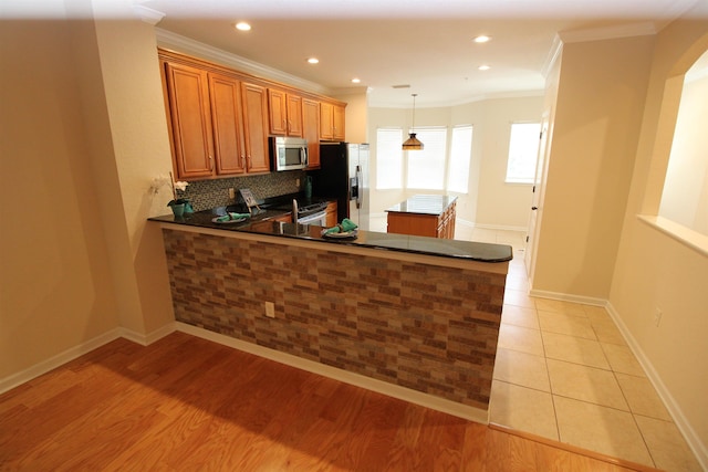 kitchen featuring crown molding, tasteful backsplash, a peninsula, appliances with stainless steel finishes, and brown cabinets