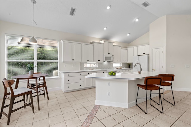 kitchen with light tile patterned flooring, white appliances, a kitchen island with sink, and white cabinets