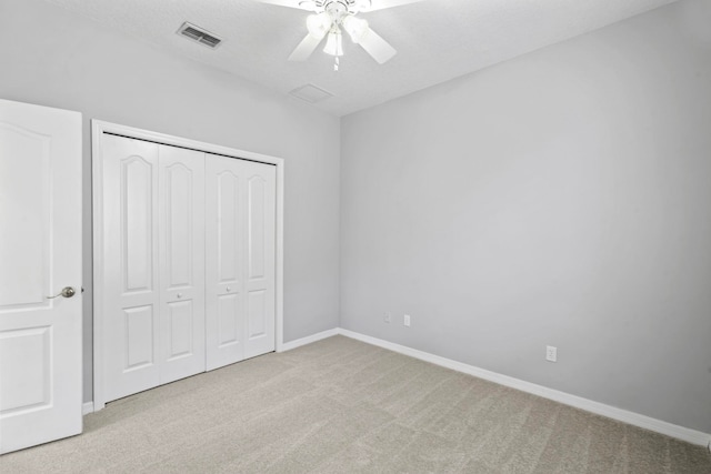 unfurnished bedroom with a textured ceiling, light colored carpet, a closet, and ceiling fan