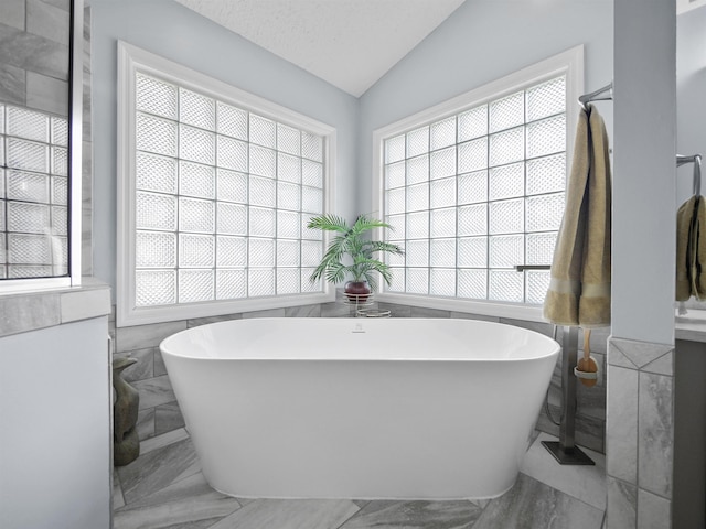 bathroom featuring a washtub, lofted ceiling, and tile walls