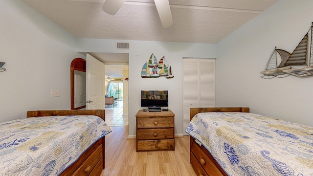 bedroom with ceiling fan, a closet, light hardwood / wood-style floors, and a textured ceiling