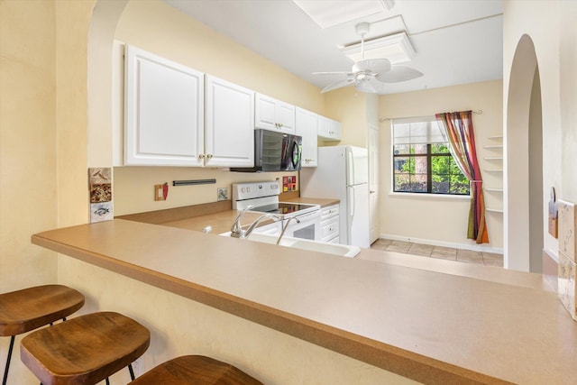 kitchen with white appliances, a ceiling fan, arched walkways, a sink, and white cabinets