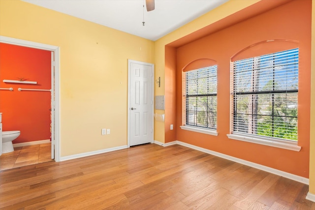 unfurnished bedroom with ensuite bath, wood finished floors, and baseboards