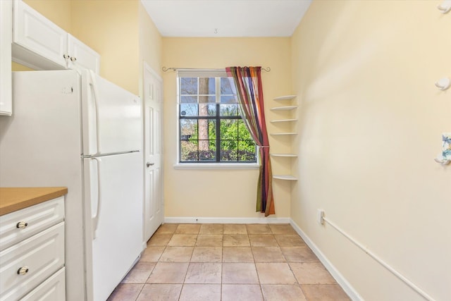 kitchen with white cabinets, light tile patterned flooring, baseboards, and freestanding refrigerator