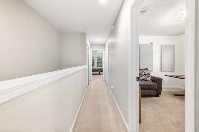 hallway featuring baseboards, visible vents, and light colored carpet