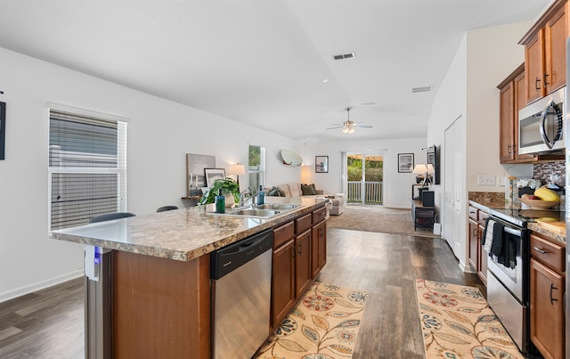 kitchen with a sink, stainless steel appliances, dark wood finished floors, an island with sink, and open floor plan