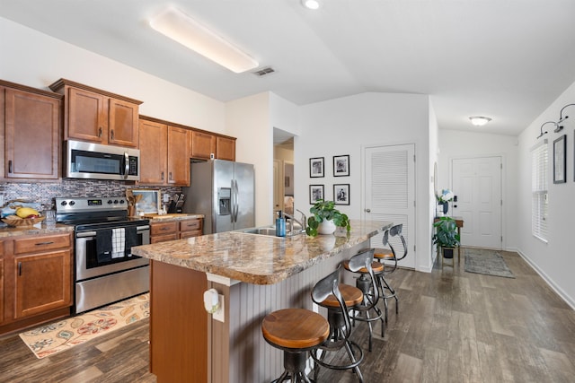 kitchen with vaulted ceiling, stainless steel appliances, dark wood-type flooring, and a breakfast bar