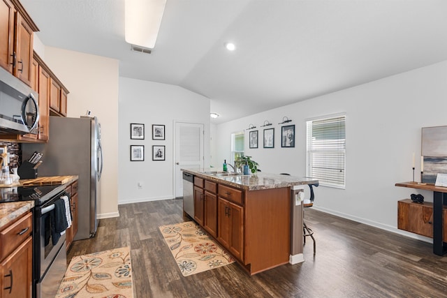 kitchen featuring a sink, stainless steel appliances, brown cabinets, vaulted ceiling, and an island with sink