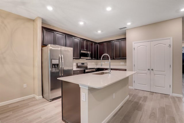 kitchen with a center island with sink, sink, appliances with stainless steel finishes, dark brown cabinets, and light hardwood / wood-style floors