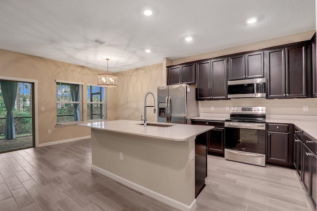 kitchen with a chandelier, appliances with stainless steel finishes, hanging light fixtures, and a kitchen island with sink