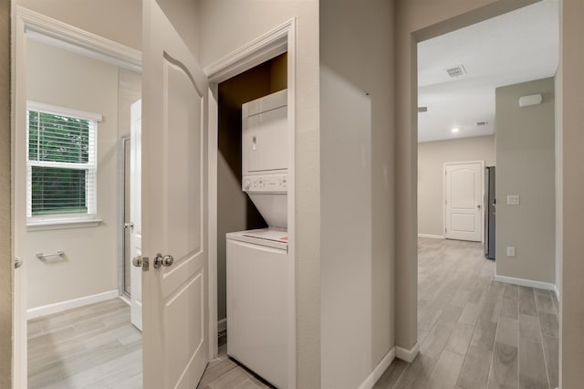 clothes washing area featuring light hardwood / wood-style flooring and stacked washing maching and dryer