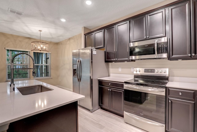 kitchen featuring appliances with stainless steel finishes, dark brown cabinets, sink, a chandelier, and hanging light fixtures