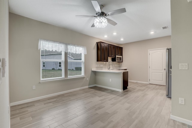 kitchen with a kitchen breakfast bar, kitchen peninsula, dark brown cabinetry, and light wood-type flooring