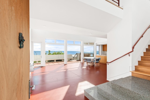 interior space featuring plenty of natural light, a water view, a towering ceiling, and concrete flooring